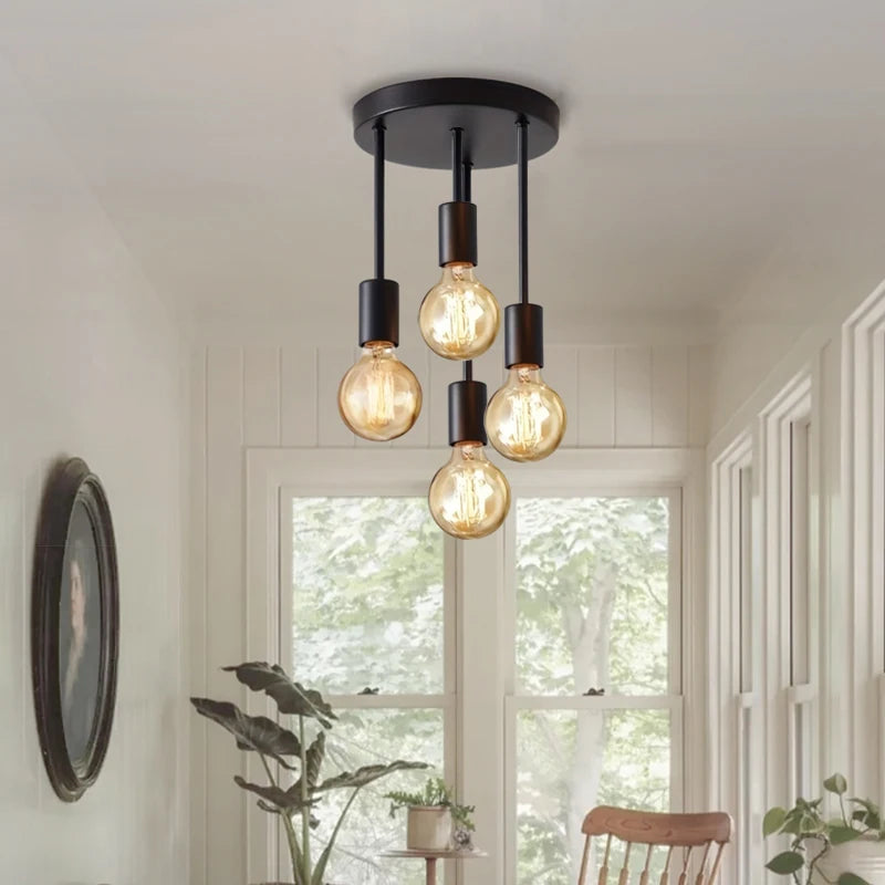 Modern black ceiling chandelier with four hanging E27 Edison bulbs, mounted on a round canopy in a bright minimalist room.